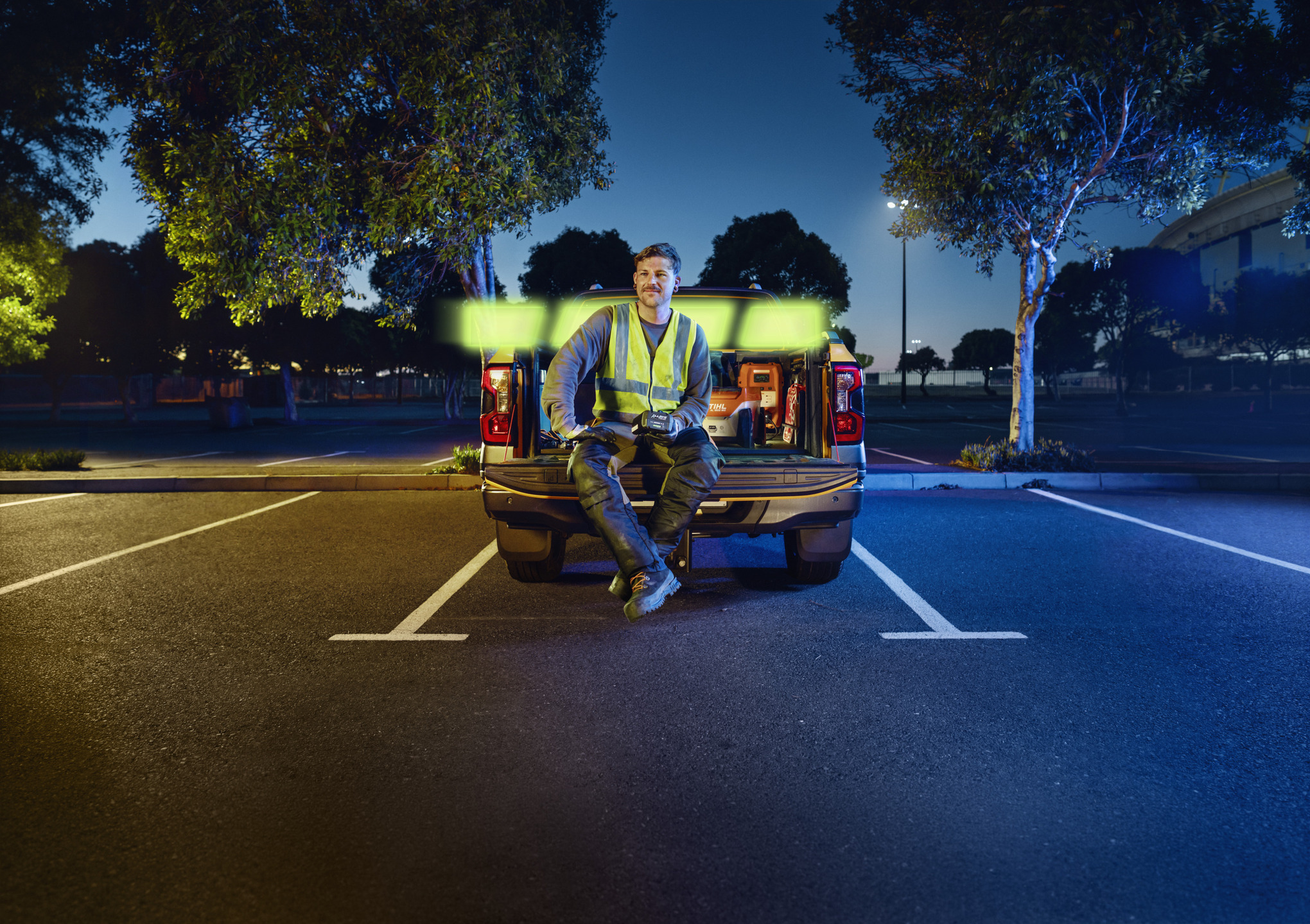  Paysagiste professionnel assis sur la benne d'un pick-up et tenant une batterie ALLPRO STIHL AP 300.0 P C