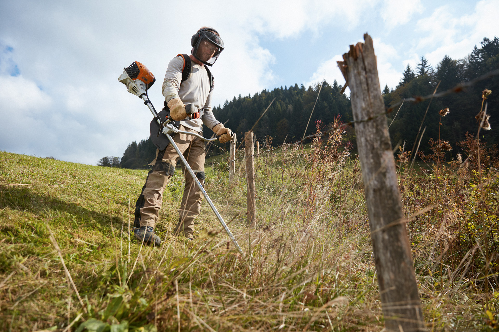 Un homme en équipement de protection fauche le gazon avec un coupe-bordures à essence STIHL FS 91