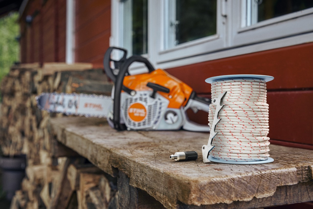 des pièces détachées et une tronçonneuse STIHL posés sur le rebord d'une fenêtre au dessus d'un tas de bois de chauffe