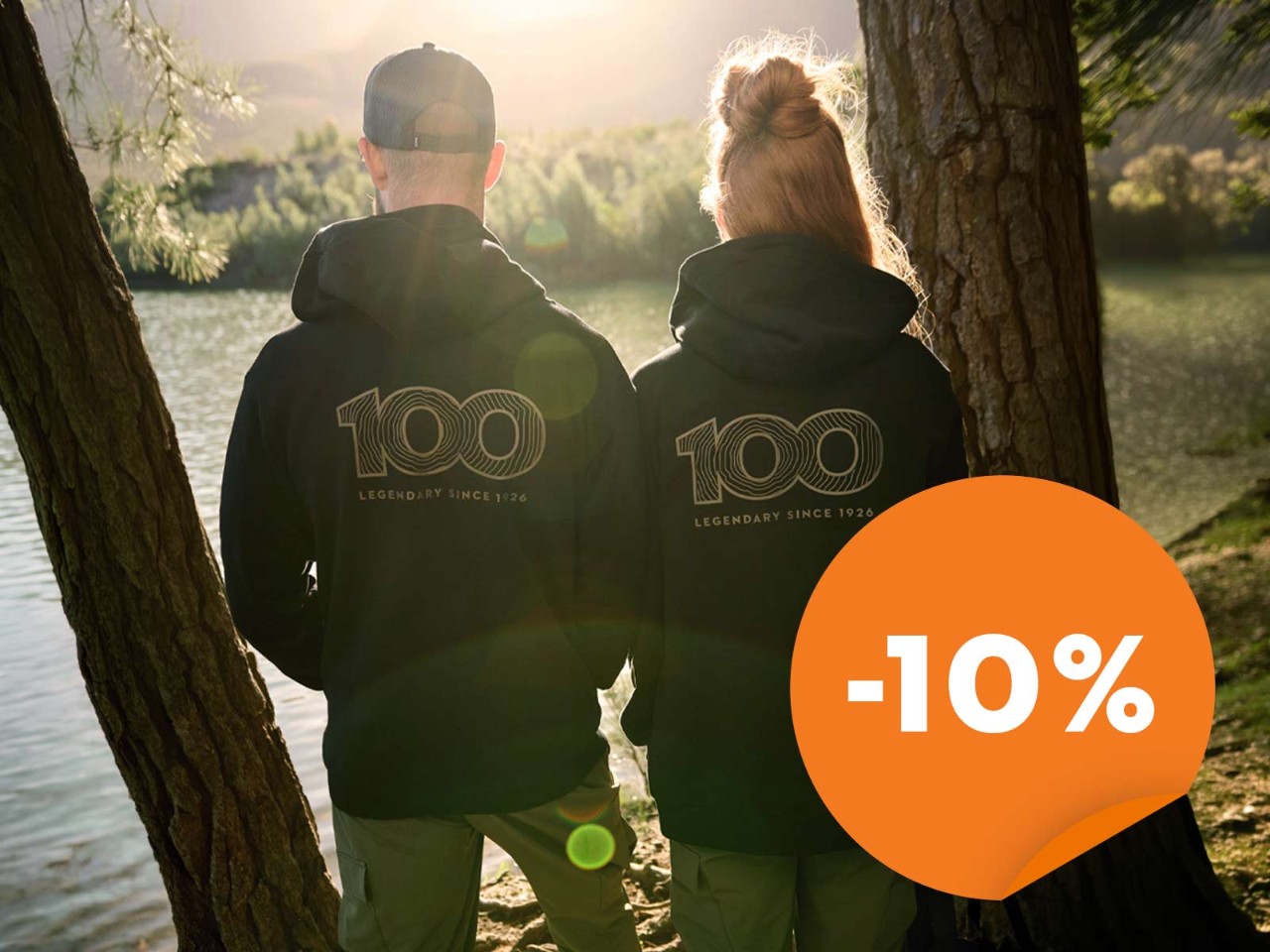un couple de dos regarde le soleil se coucher au bord d'un lac avec un sweat shirt STIHL 100 ans