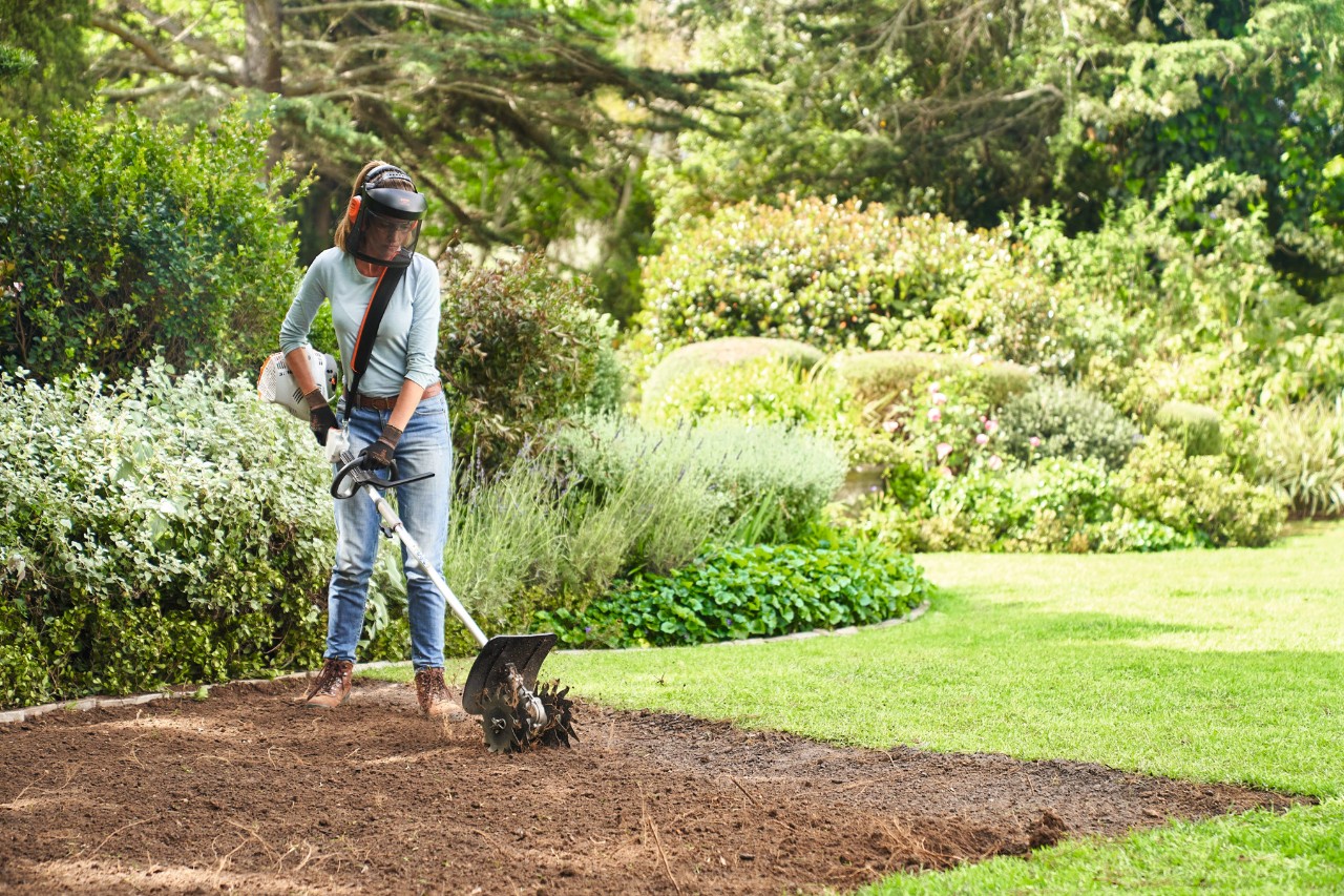 Une femme utilise le moteur combisystème STIHL KM 56 RC-E avec une sarcleuse pour préparer le sol pour le gazon en rouleau