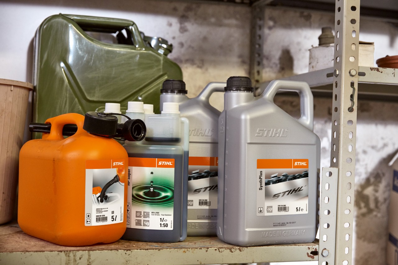 Un ensemble de bidons comprenant un grand jerrican en acier, une bouteille d’huile pour mélange moteur à 2 temps STIHL HP Super et un bidon combiné orange