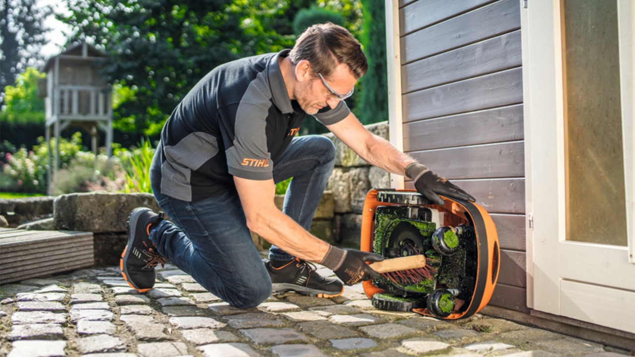 Un homme qui nettoie son robot tondeuse STIHL RMI
