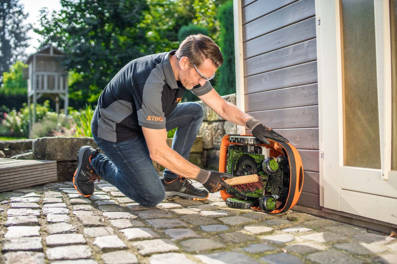 Un homme utilisant une brosse pour nettoyer le dessous d’un robot de tonte STIHL iMOW® RMI 422