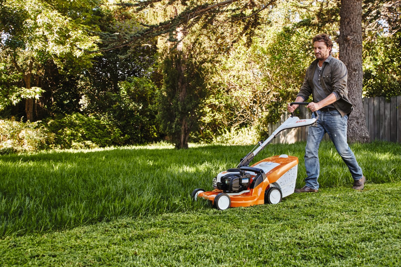 Un homme tond la pelouse dans un jardin avec une tondeuse à gazon STIHL 