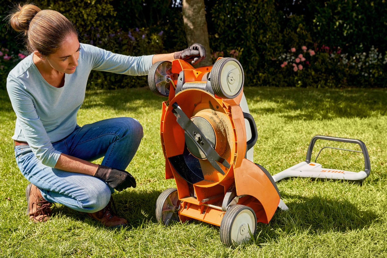 Une femme regarde sous sa tondeuse à batterie STIHL RMA 339C dans son jardin