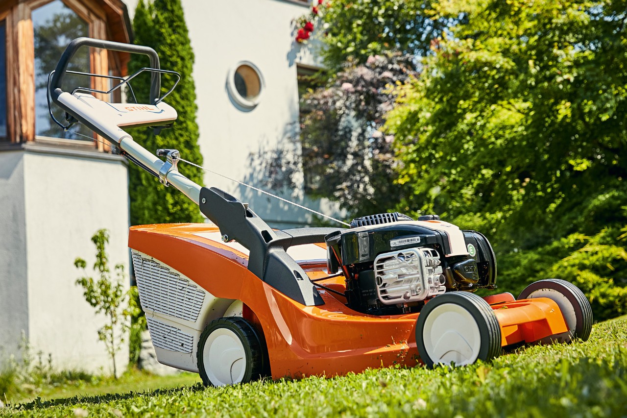 Tondeuse thermique STIHL RM 443 T sur un gazon vert devant une maison 