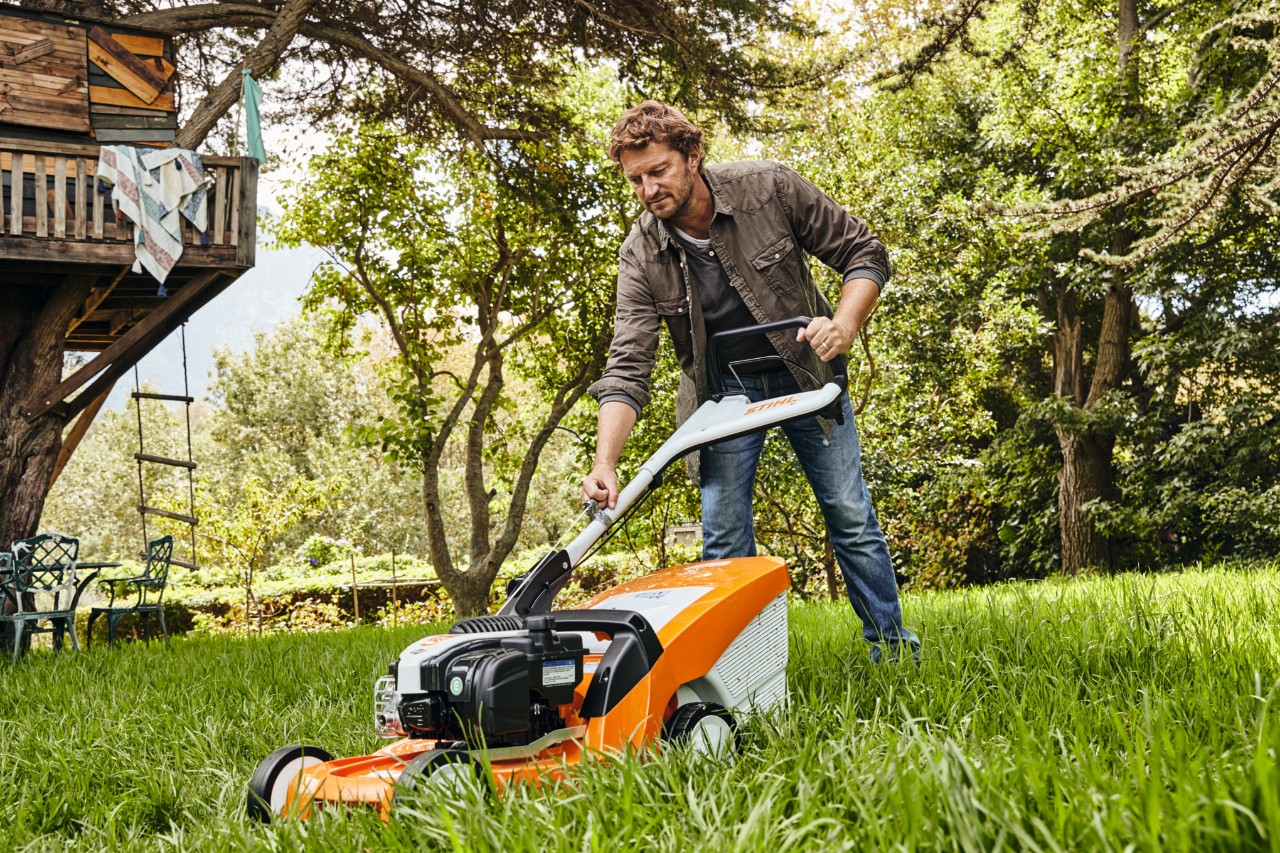 Un homme, dans un jardin, tirant sur la corde de démarrage de la tondeuse à essence STIHL RM 448 TC pour la démarrer