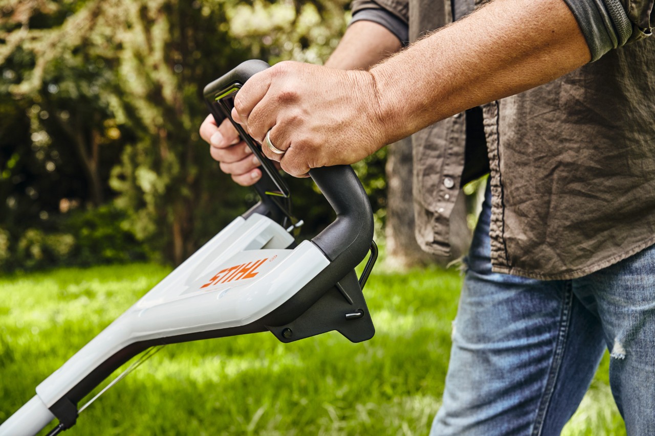 Un homme en train de tenir la tondeuse à essence STIHL RM 448 TC au niveau du guidon pour tondre la pelouse