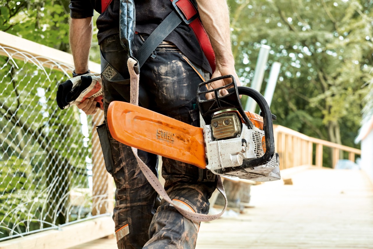 Un homme traverse un pont et porte une tronçonneuse thermique STIHL MS 261 munie d’un protège-chaîne
