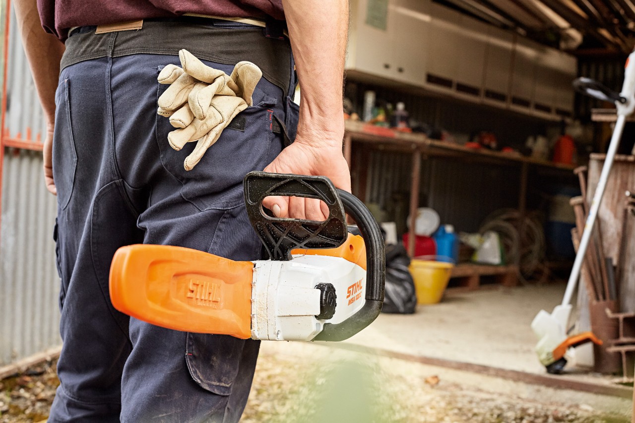 Un homme tient une tronçonneuse sur batterie STIHL munie de son protège-chaîne et se dirige vers un atelier