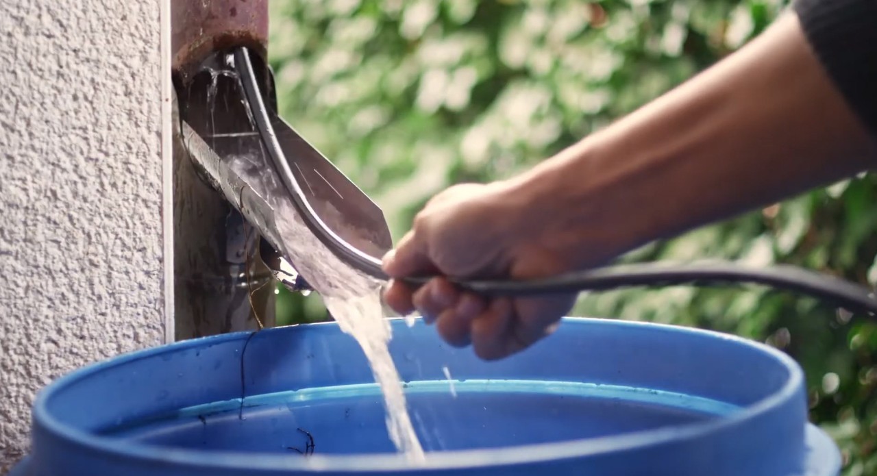 Une tige métallique flexible est glissée dans le tuyau de descente pour nettoyer l’arrivée bouchée d’une tonne d’eau de pluie bleue