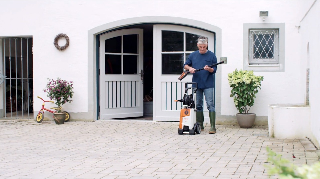 Un homme se tient devant une maison blanche et prépare un nettoyeur haute pression STIHL pour nettoyer la façade