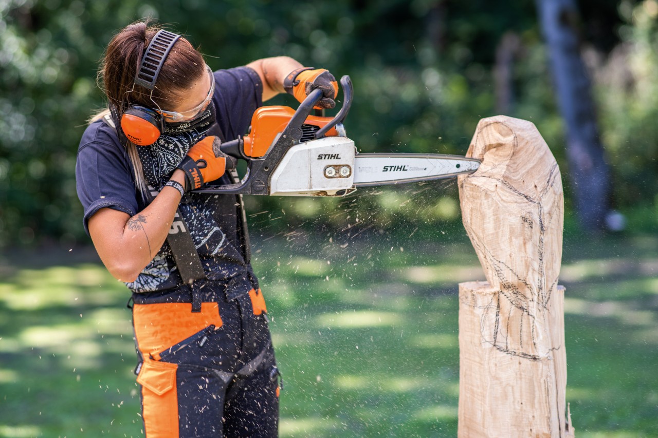 Femme avec protection auditive STIHL lors de la sculpture d’une chouette en bois avec une tronçonneuse