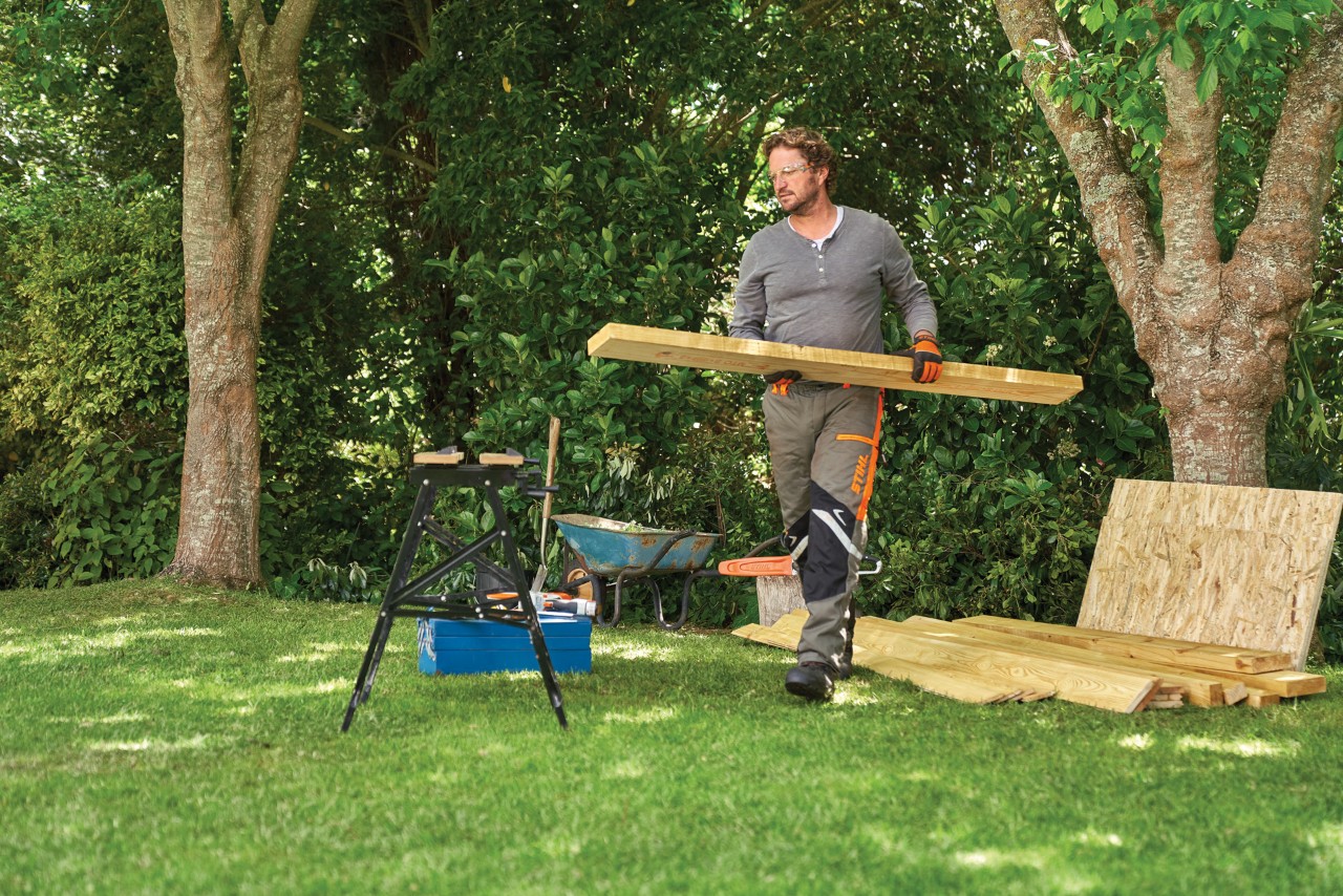 Comment construire un abri de jardin : personne prenant une planche dans une pile de bois sous un arbre