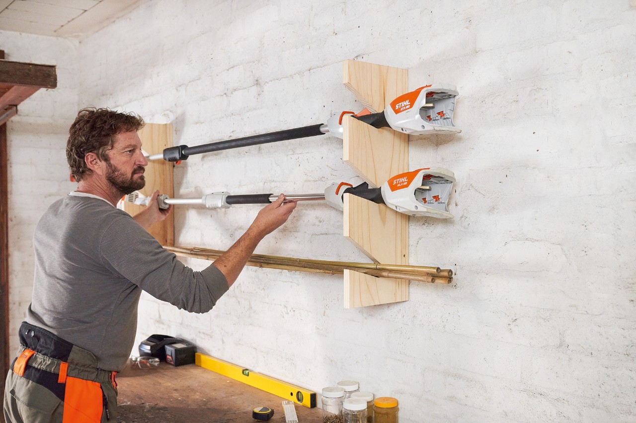 Homme place une débroussailleuse STIHL dans un support de rangement pour outils de jardin qu’il a fabriqué 