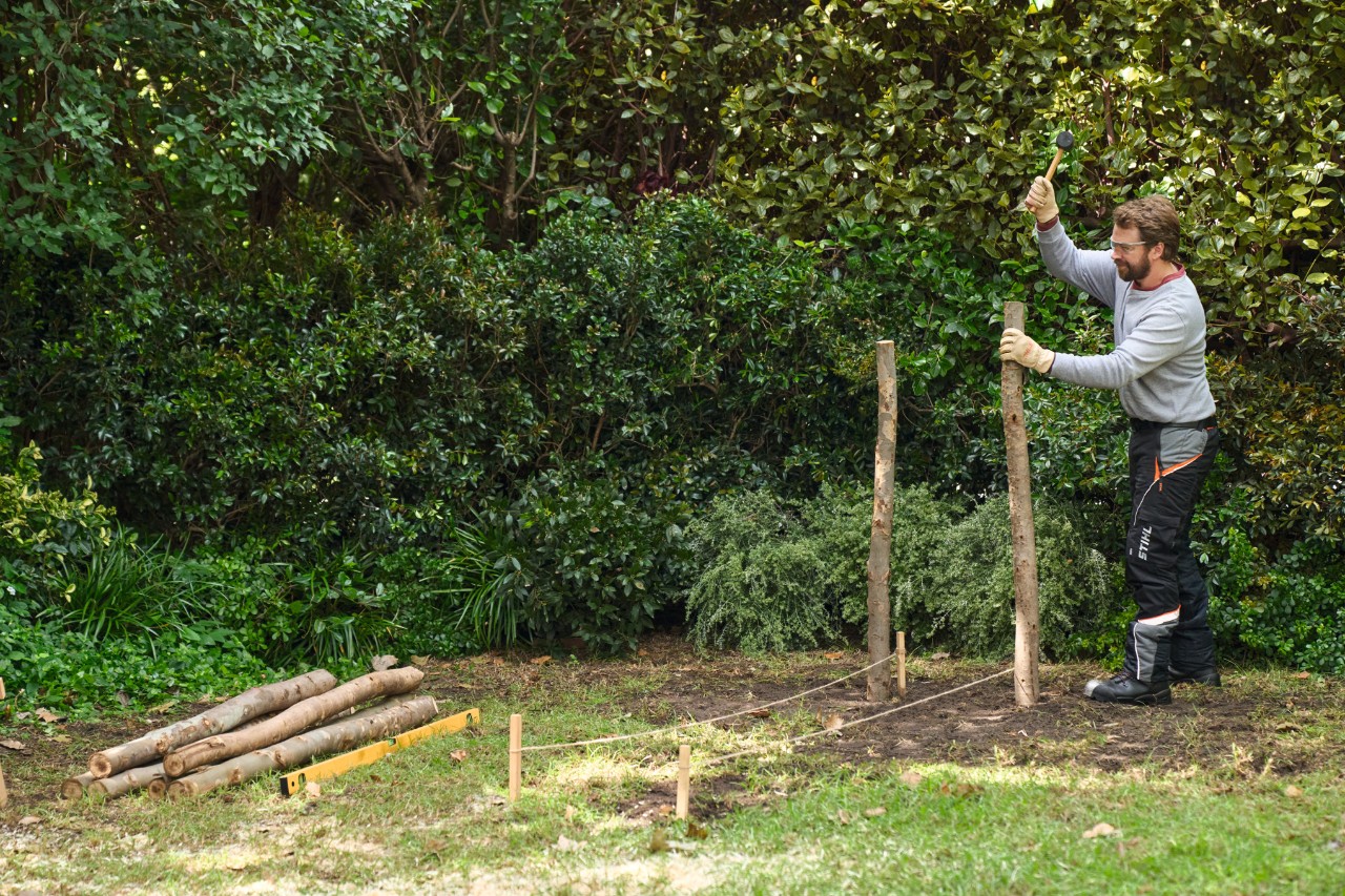Homme enfonçant deux piquets en bois pour définir les angles de la haie sèche
