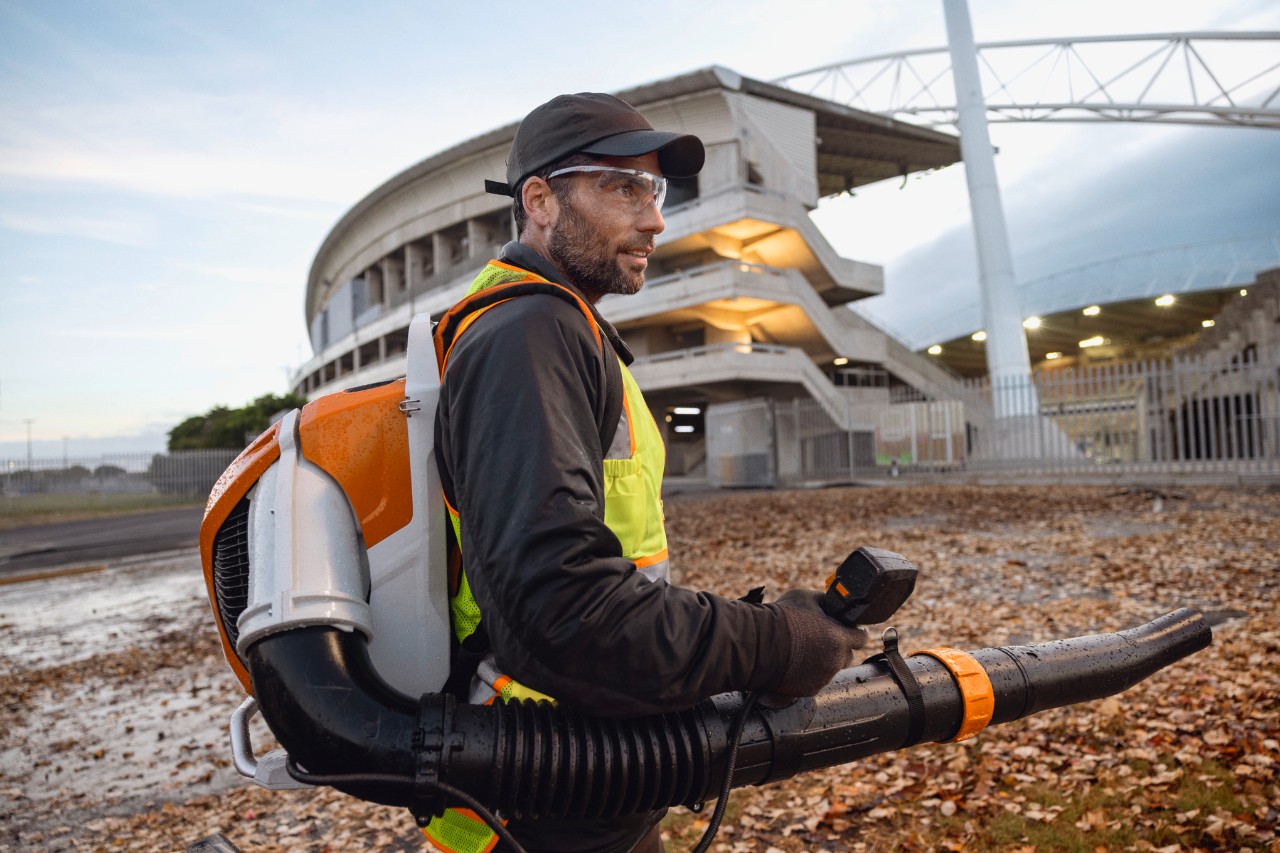 Tard dans la soirée, une personne nettoie les feuilles et les débris d'un stade à l'aide du souffleur de feuilles sans fil ALLPRO STIHL BRA 600.