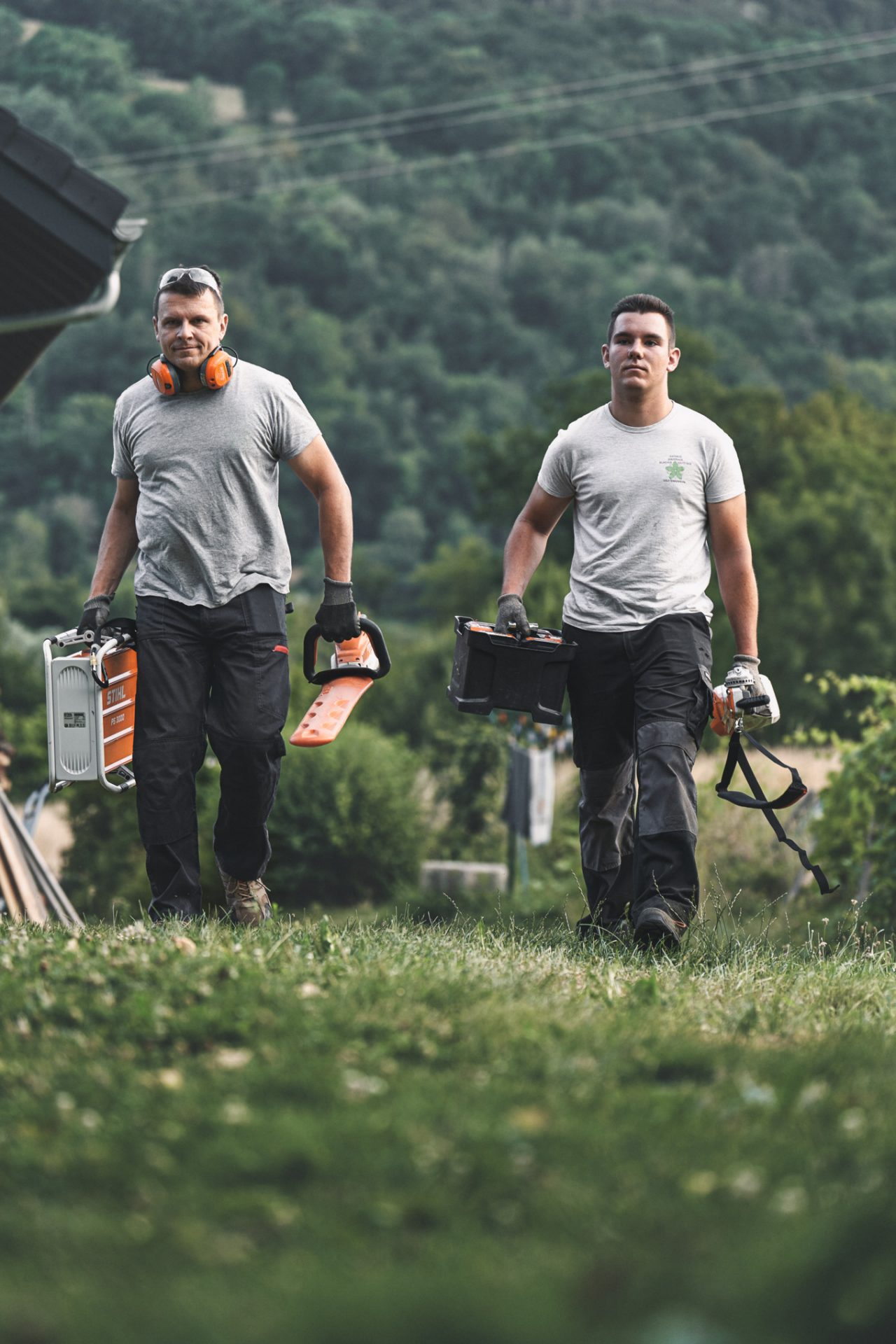 Deux professionnels marchant dans une prairie avec des appareils à batterie STIHL