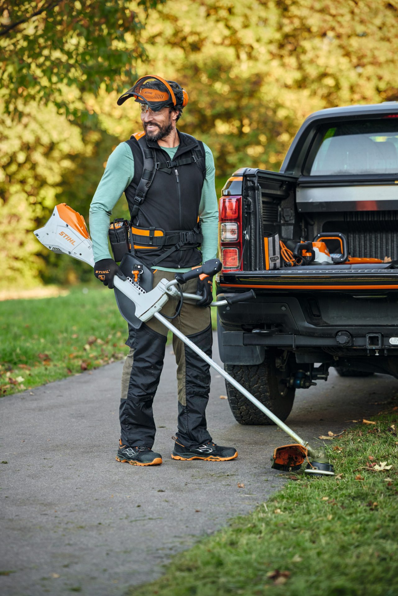 Homme avec le kit FS et une débroussailleuse à batterie STIHL FSA 200 devant une voiture
