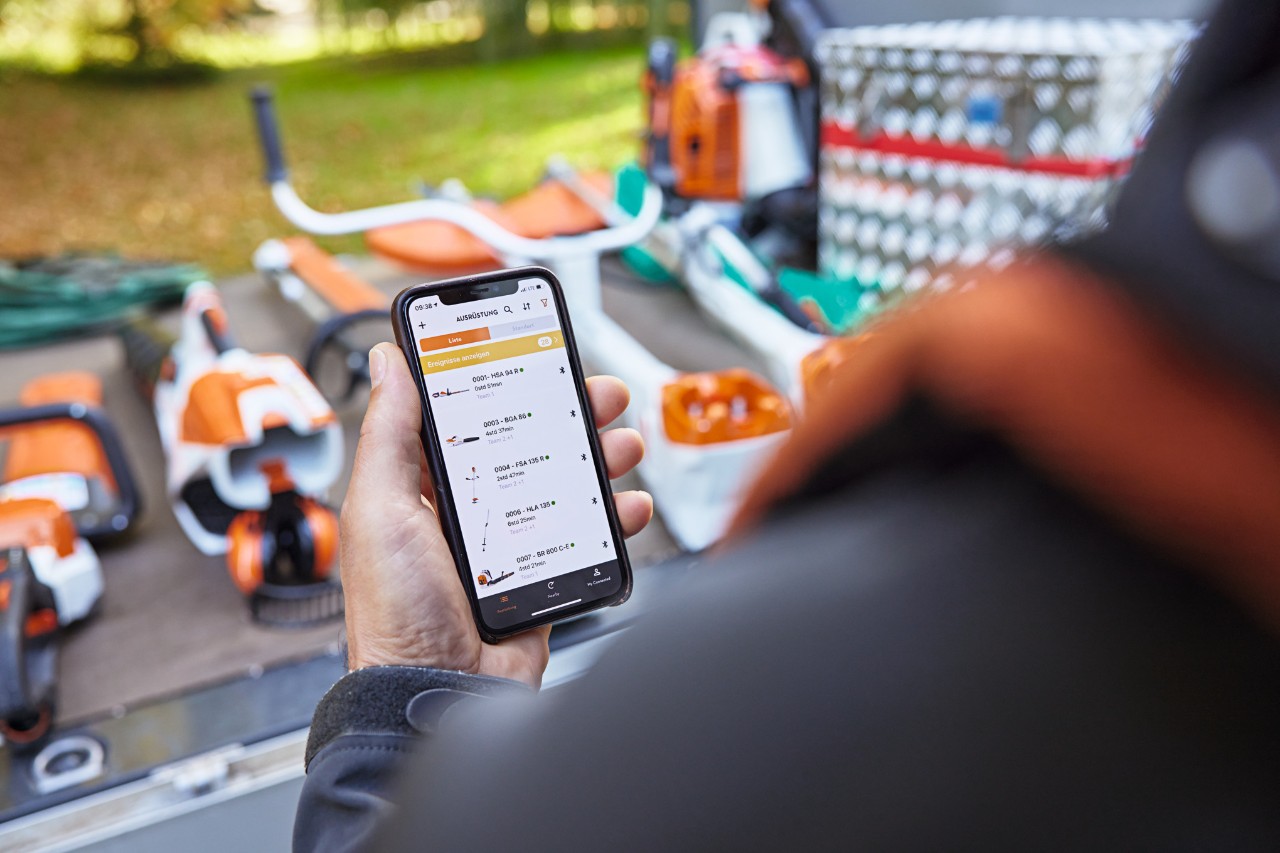 Quelqu’un tenant un smartphone avec l'appli STIHL connected devant un véhicule avec divers appareils STIHL