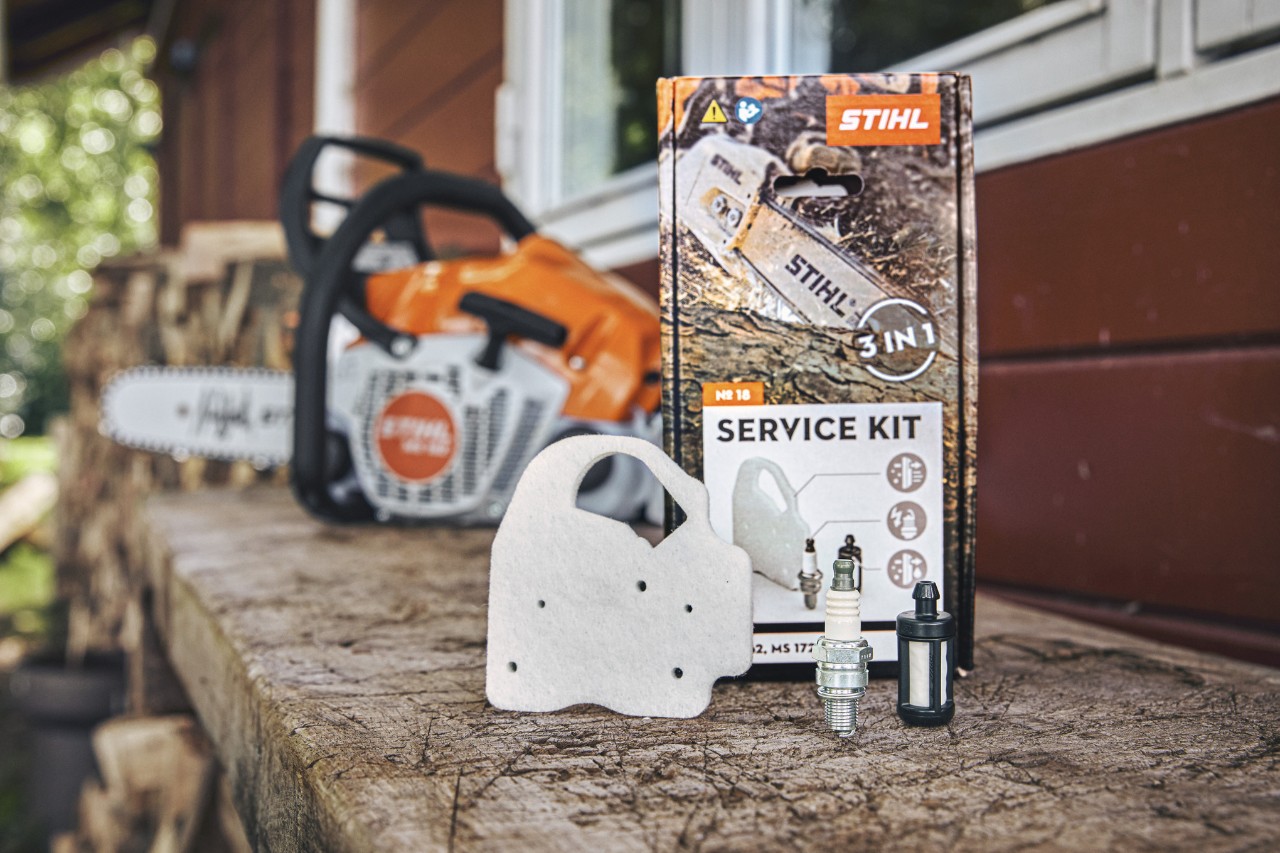 Kit d’entretien STIHL 18 sur un établi, différents composants posés devant : filtre à air non-tissé, bougie et filtre à carburant