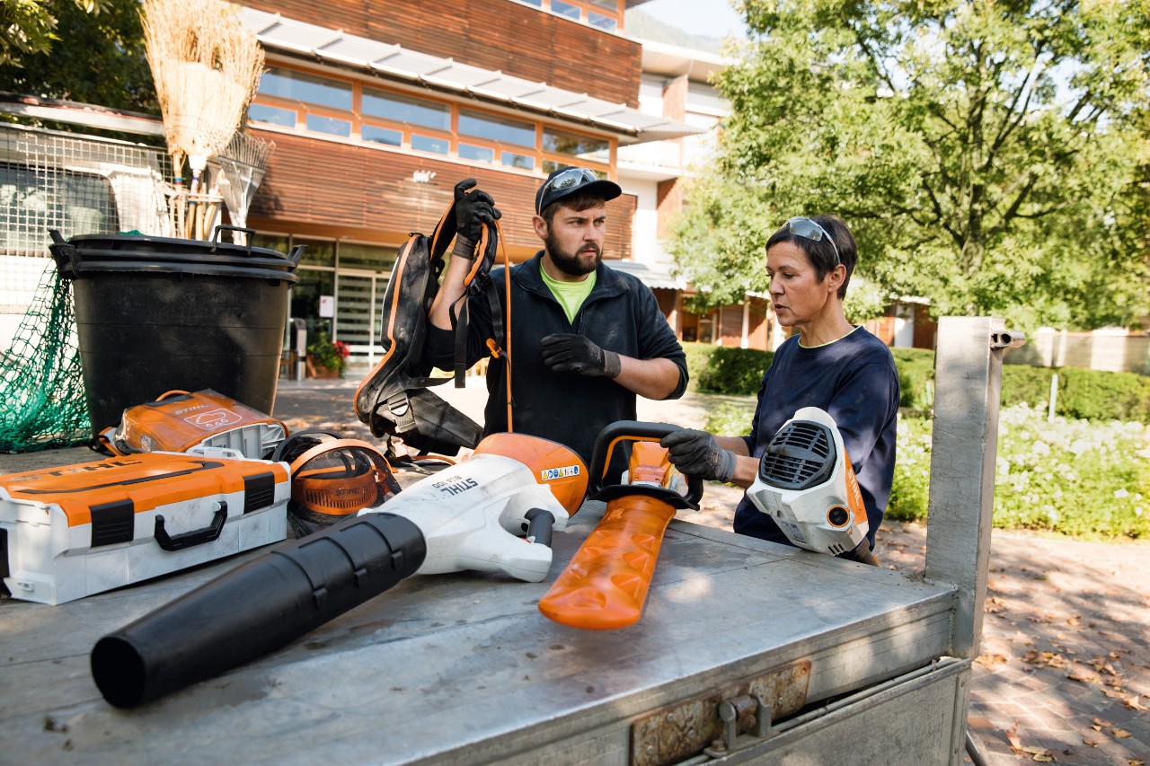 Une femme et un homme portant des gants et des lunettes de protection et discutant devant un camion sur lequel sont posés des appareils motorisés STIHL.