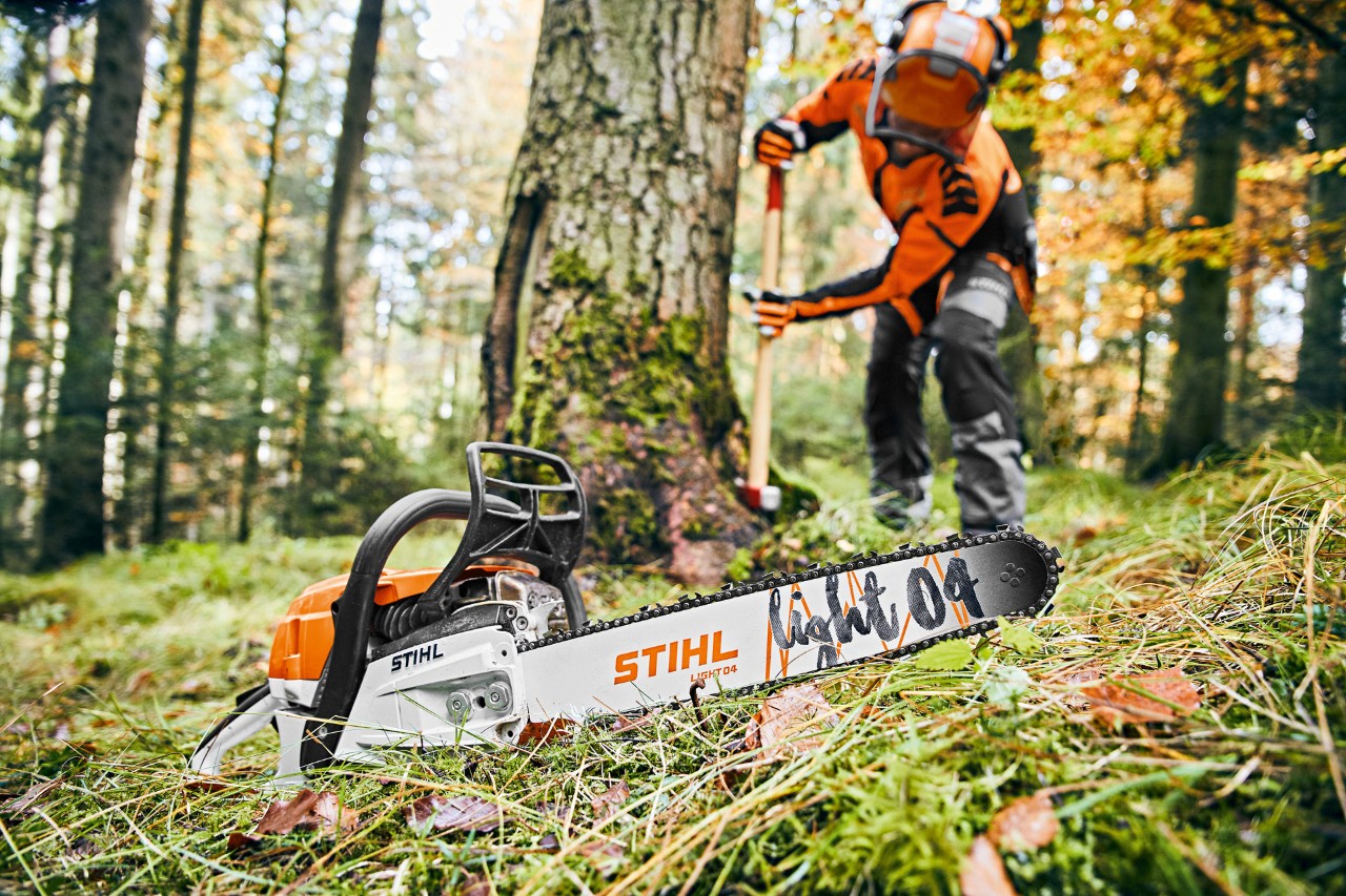 Homme en équipement de protection dans la forêt, au premier plan une tronçonneuse à essence STIHL MS 261 C-M avec guide-chaîne Light 04