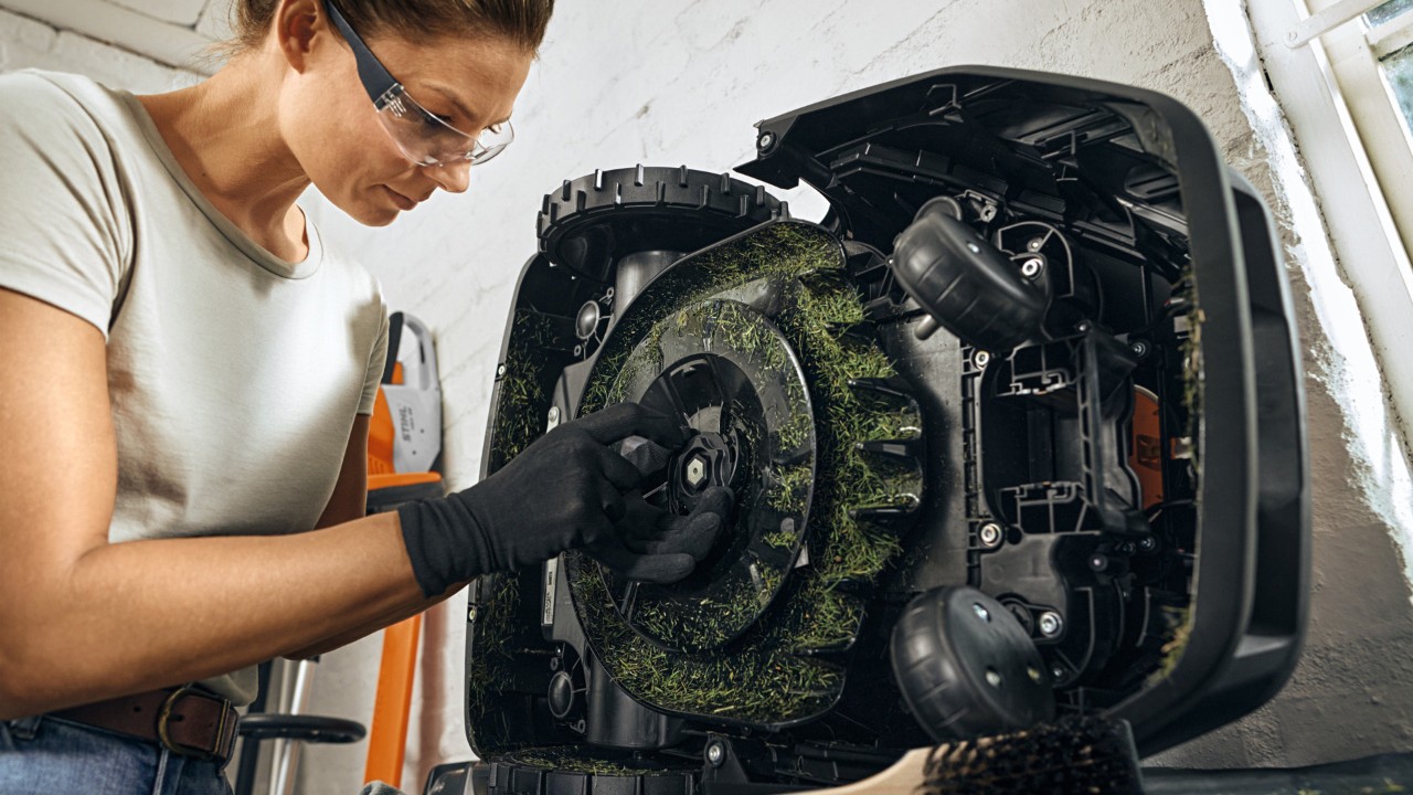 Une femme qui change les lames de son robot tondeuse STIHL