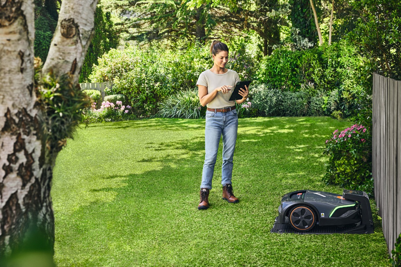 Une femme utilise la STIHL iMOW® EVO via une tablette dans son jardin