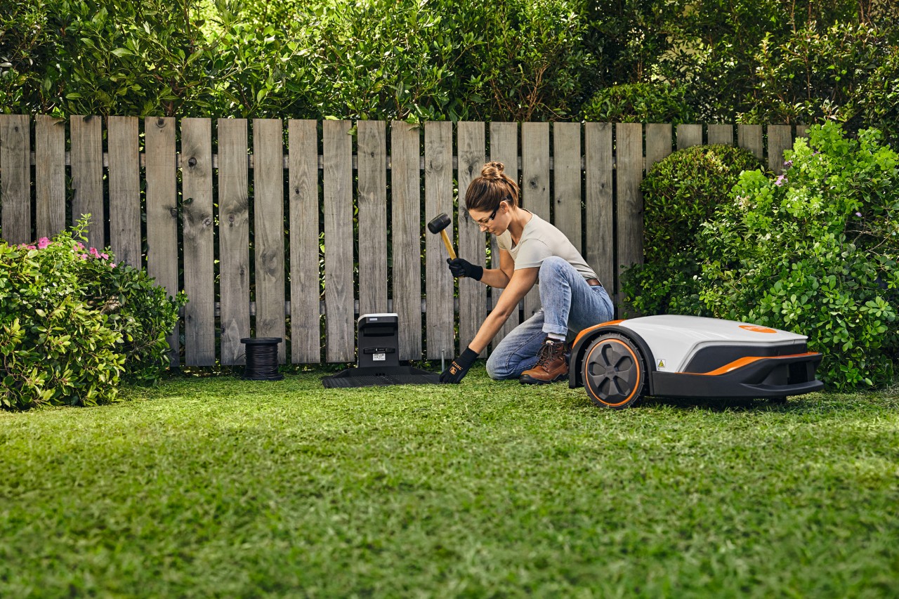 Femme installant elle-même la station de base pour sa STIHL iMOW® devant une clôture dans son jardin.